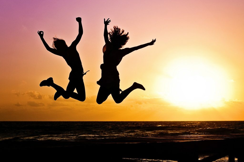 Two women jumping for joy on a beach with the sunset behind them